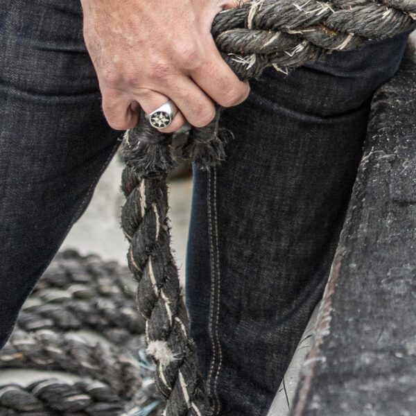 Signet ring with wind rose, compass motif, worn by sailors holding a rope on deck. From Neptune Jewels.