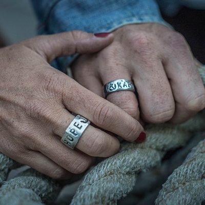 Ein Paar hlt sich die Hände. Sie tragen Bandringe mit personalisierter Wunschprägung, hergestellt von Neptunsgeschmeide.