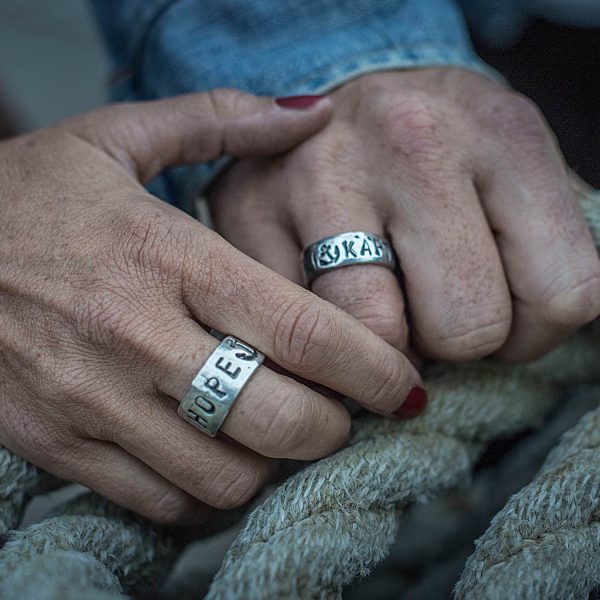 Een paar houdt elkaars hand vast. Ze dragen bandringen met gepersonaliseerde embossing, gemaakt door Neptunsgems.