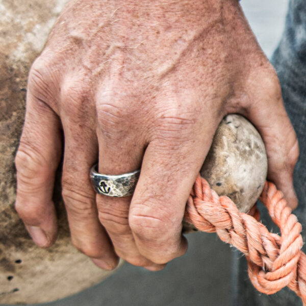 Anillo de banda con joyería de Neptuno en relieve de ancla. Usado en una mano sujetando un guardabarros.