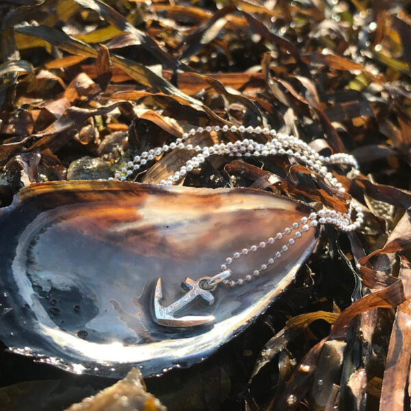 Halsschmuck Ankerchen 11 mm an Kette. Ankeranhänger an Silberkette, liegt in einer Muschel auf Algen am Strand, von Neptunssgeschmeide.