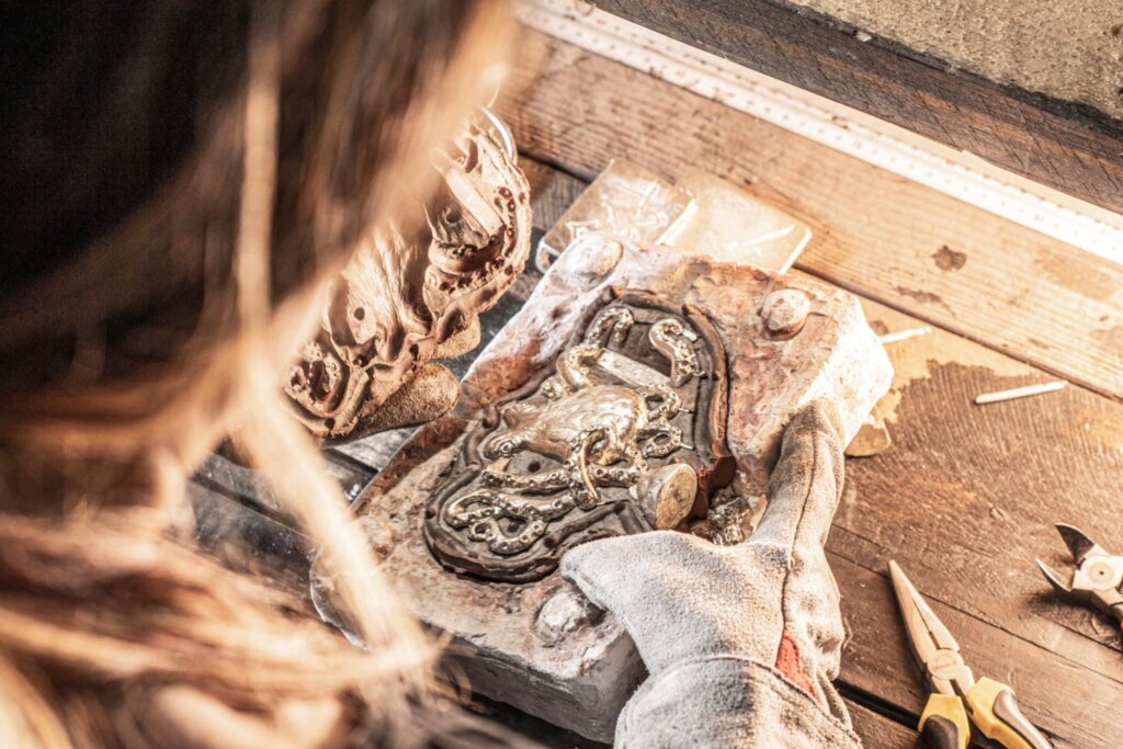 Neptunsgeschmeide Werkstatt und Atelier: Entformung eines Zinngusses einer Krake oder Oktopus Motiv Gürtelschnalle per Hand. Detailaufnahme.