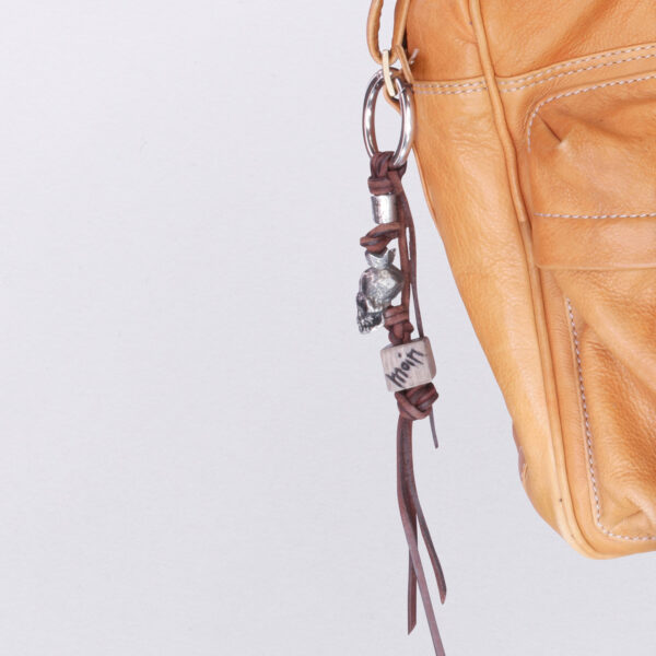 Gebamsel® Anhänger Totenkopf König Holzwürfel, Ansicht seitlich an Beispieltasche, von Neptunsgeschmeide. Taschen- oder Schlüsselanhänger mit Karabinerhaken, groß.