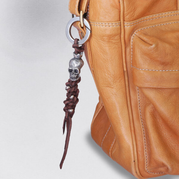 Gebamsel® Anhänger Totenkopf Silberperlen, Ansicht an brauner Ledertasche, von Neptunsgeschmeide. Taschen- oder Schlüsselanhänger mit Karabinerhaken gerade Kanten, klein.