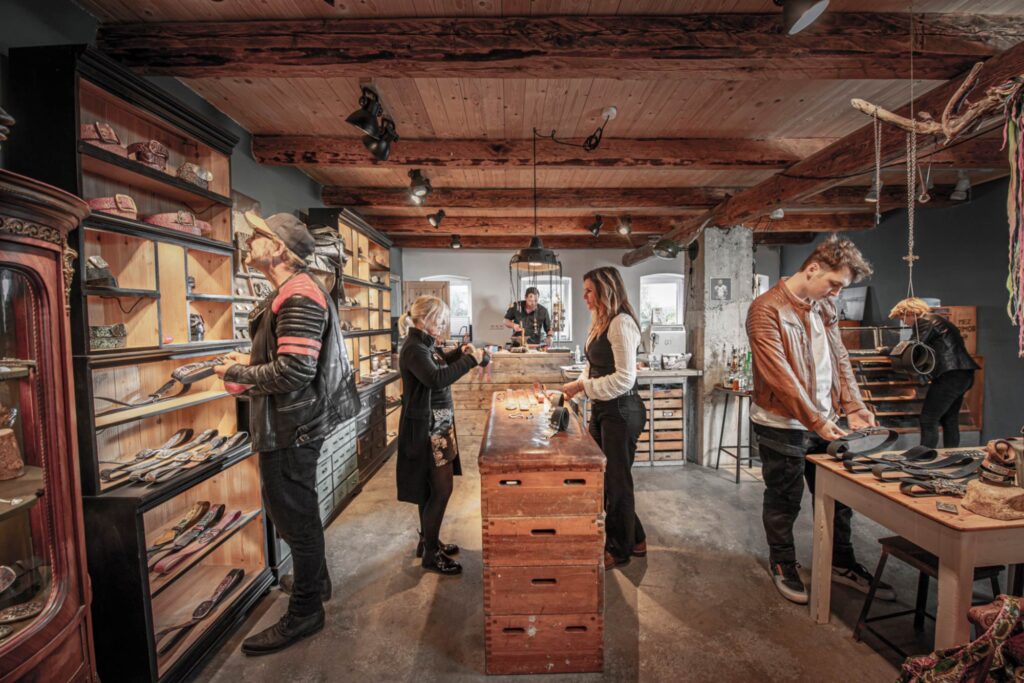 Neptunsgeschmeide Showroom. Ladenbereich, Kunden betrachten die ausgestellten Waren. Jen Wolke berät Kundin. Im Hintergrund Martin Wolke in der Werkstatt der Scheune in Stampe.