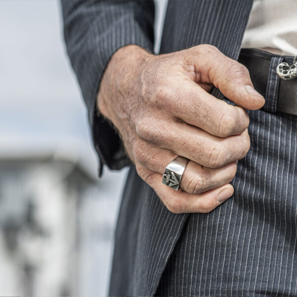 Signet ring with anchor motif, blackened. Size approx. 16 x 25 mm, made of Neptune jewelry. Promotional image of ring on hand, male person in suit. Detail view hand.