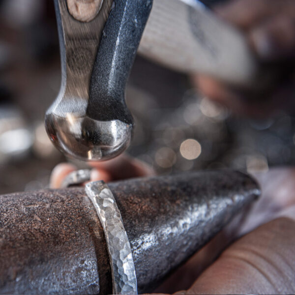 Producción de un brazalete, superficie martillada, la imagen muestra el martillo golpeando el brazalete y creando una estructura ondulada. De Neptuno Joyas.