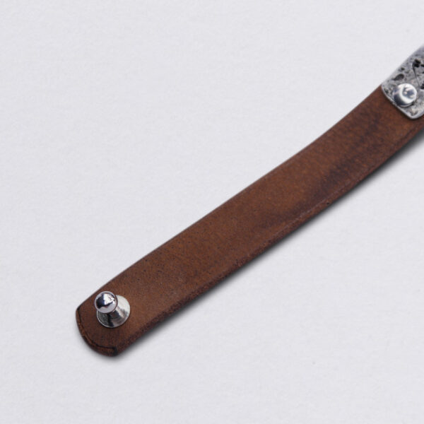 Lederarmband Motto "Niemals zurück" auf Zinnplättchen von Neptunsgeschmeide. Detailbild Knopfniete Verschluss..