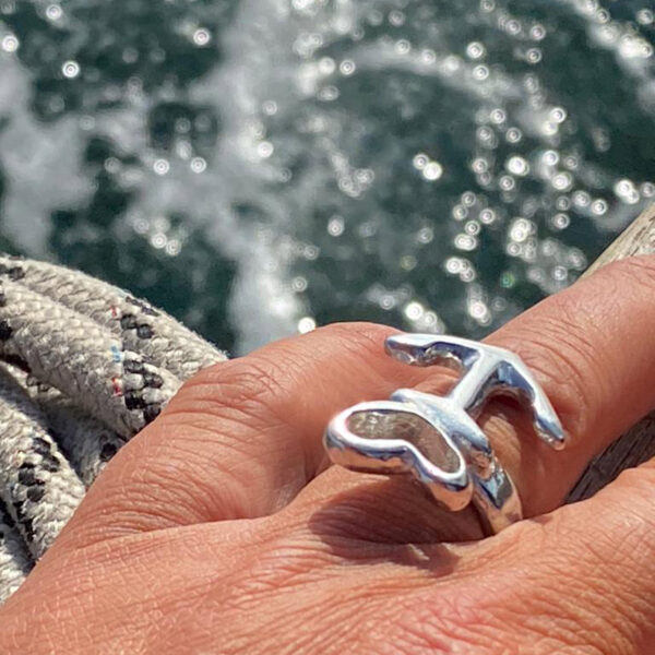 Motif ring heart anchor freestanding, pewter or silver, handmade by Neptune jewelry with optional embossing on the outside. Detail picture Motif ring on hand over the edge of the harbour. Close detail image.