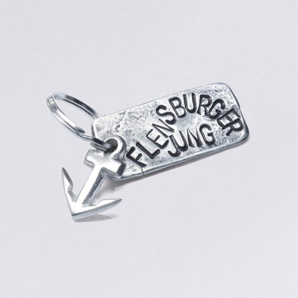 Key ring with Flensburger Jung embossing with a small anchor, dimensions: approx. 2 x 4,5 cm, from NeptunsSchmeide. Customizable with desired embossing.