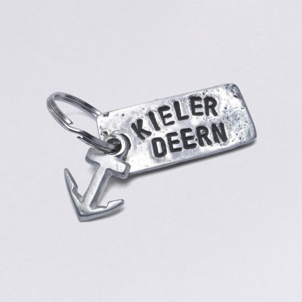 Key ring with embossing Kieler Deern with a small anchor, dimensions: approx. 2 x 4,5 cm, from NeptunsSchmeiße. Customizable with desired embossing.