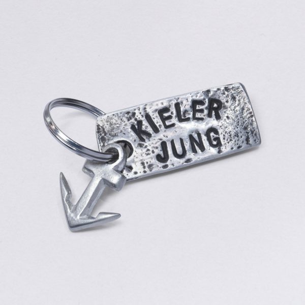 Key ring with embossing Kieler Jung with a small anchor, dimensions: approx. 2 x 4,5 cm, from NeptunsSchmeiße. Customizable with desired embossing.