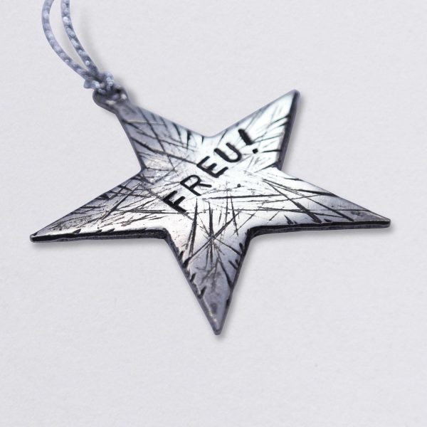 Baumschmuck Stern Freu!, Weihnachtsstern mit Frecher Textprägung und mit optionaler Wunschprägung aus Zinn. Maße ca. 8 x 8 cm. Von Neptunsgeschmeide. Schräge Ansicht liegend.