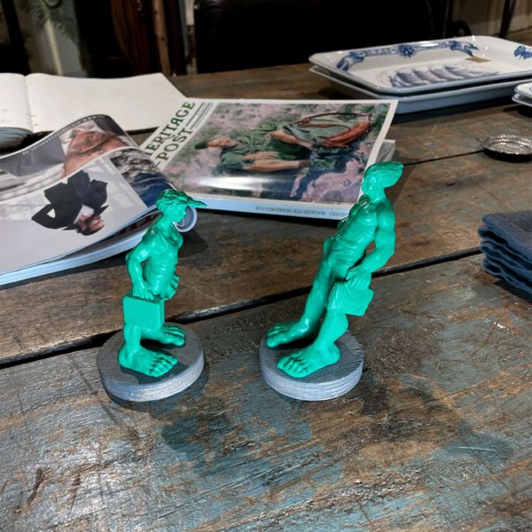 Deux miniatures de 10 cm de haut des « Géants voyageurs dans le vent » sur le parvis de la gare de Westerland à Sylt sont posées sur une table. Il y a un magazine derrière pour mieux montrer la comparaison des tailles. Les sculptures ont été réalisées par le sculpteur Martin Wolke et sont disponibles dans la boutique en ligne Neptunsgeschmeide.