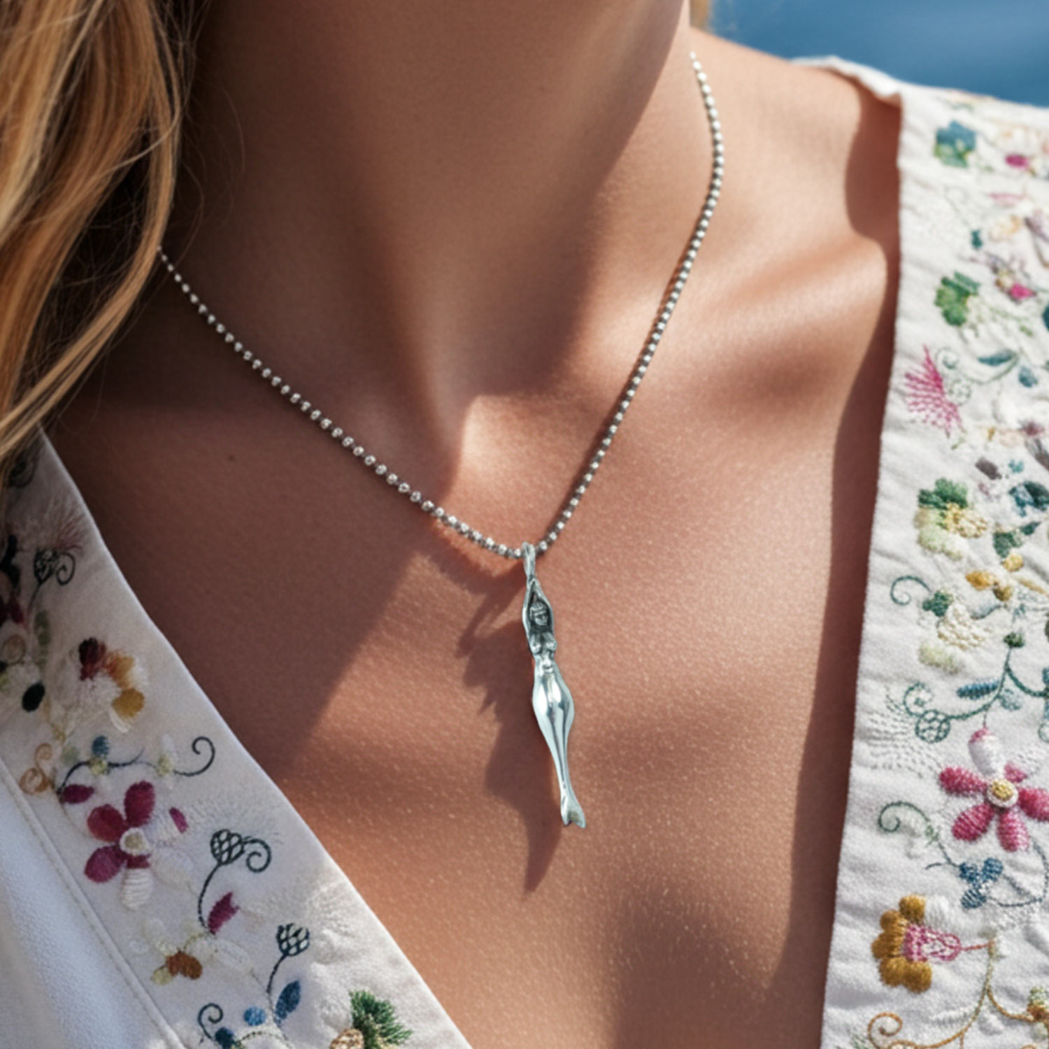 Meerjungfrau Schmuckanhänger von Neptunsgeschmeide, gefertigt in 925er-Silber. Bild zeigt Nahaufnahme im Ausschnitt einer Frau am Meer.