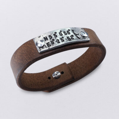Koordinaten Sylt Armband von Neptunsgeschmeide. Ein Hand-geprägtes Zinnplättchen ist auf einem Lederarmband mit Knopfnietenverschluss vernietet. Abbildung zeigt die Koordinaten von List auf Sylt.