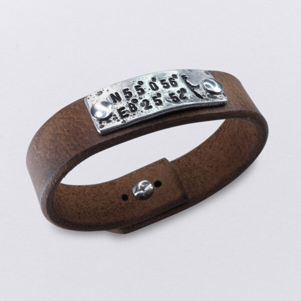 Koordinaten Sylt Armband von Neptunsgeschmeide. Ein Hand-geprägtes Zinnplättchen ist auf einem Lederarmband mit Knopfnietenverschluss vernietet. Abbildung zeigt die Koordinaten von List auf Sylt.