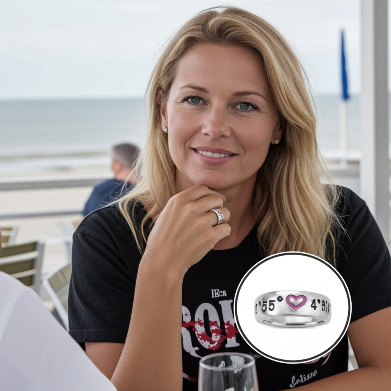 Koordinaten Bandring von Neptunsgeschmeide mit polierter Oberfläche und Herzsymbol mit pinker Gießharzfüllung. Angefertigt in Zinn. Bild zeigt Frau in einer Strandbar am Tisch, die den Ring trägt.